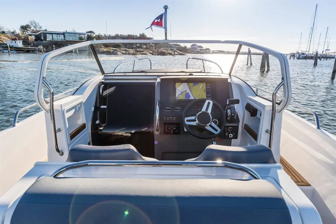 View from the helm of a boat with a steering wheel, navigation screen, and water in the background, reflecting sunlight.